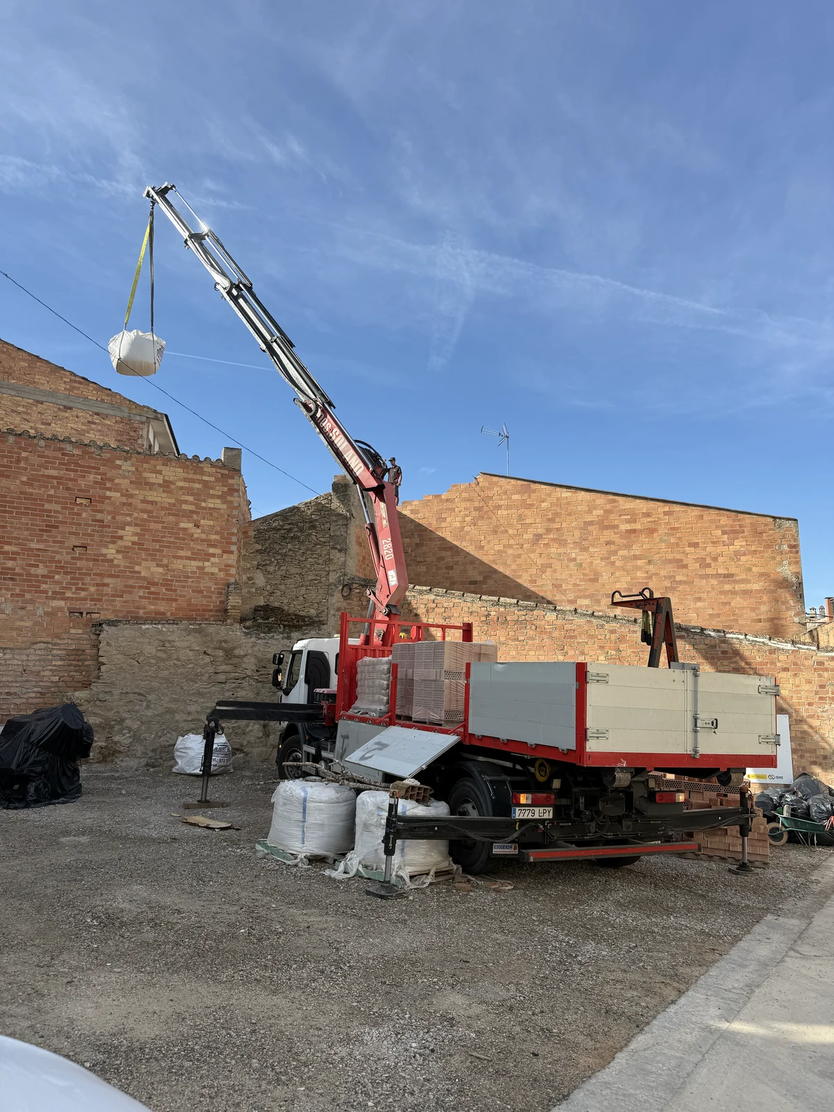 Camión grúa de Solano elevando un big bag de material por encima del muro de una obra