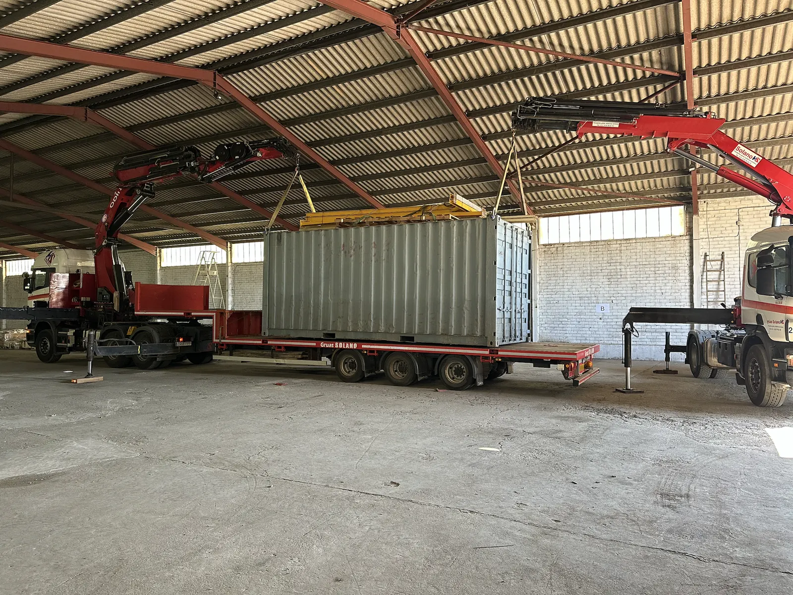 Un contenedor elevado entre dos grúas, dentro de una nave