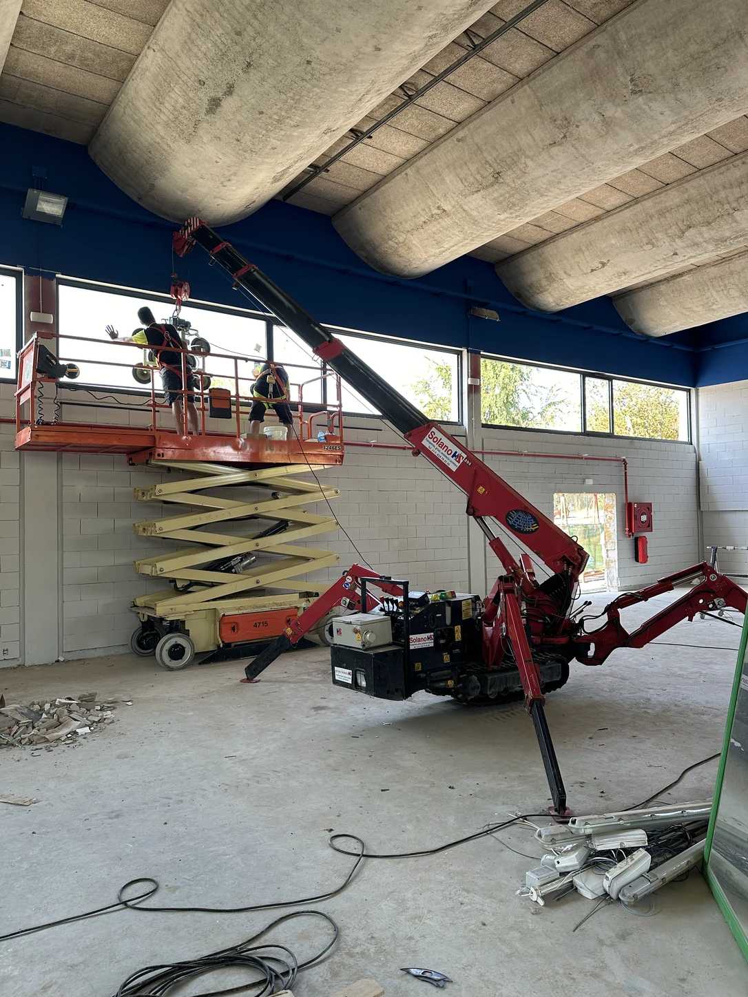 Mini grúa de orugas de Solano colocando cristales dentro de una nave, con dos operarios en plataforma elevadora