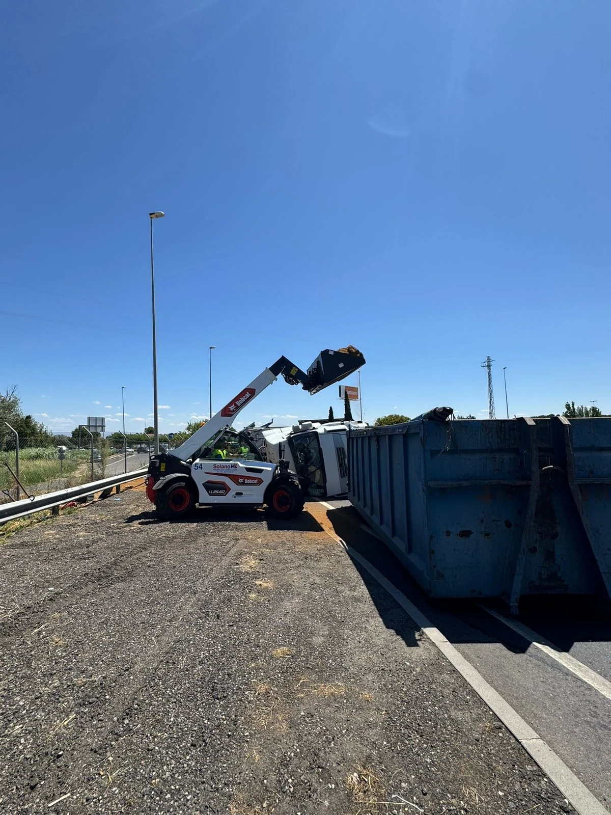 Manipulador Bobcat de Solano trasvasando la carga de un camión volcado en la autopista a un contenedor