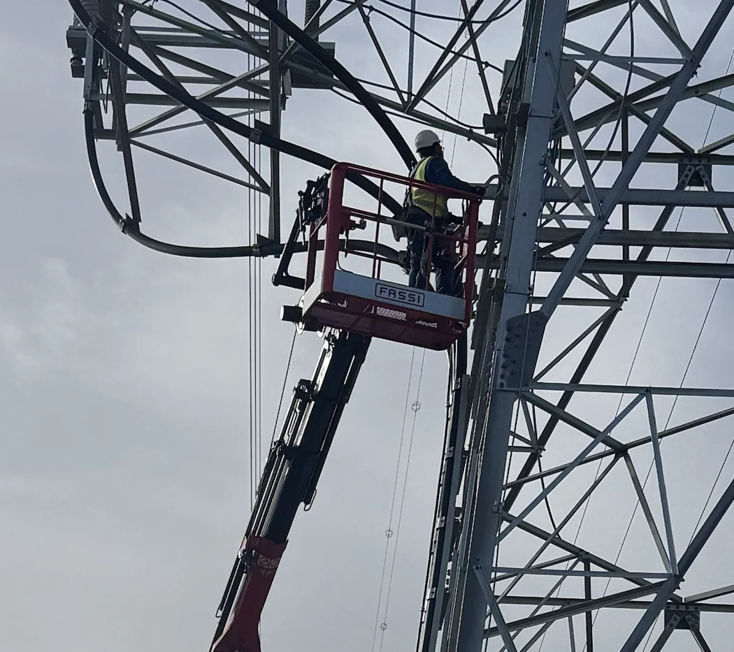 Operario con casco y chaleco trabajando desde la cesta homologada en una torre de alta tensión